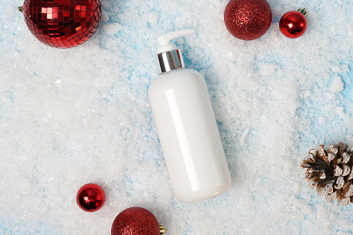 Cosmetic product lotion or shampoo on white christmas background with snow and red decorations, flat lay. Winter care