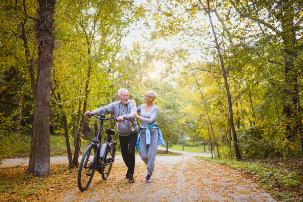 alegre pareja de ancianos activos con bicicletas caminando juntos por el parque. actividades perfectas para personas mayores. - action mature adult bicycle senior couple fotografías e imágenes de stock