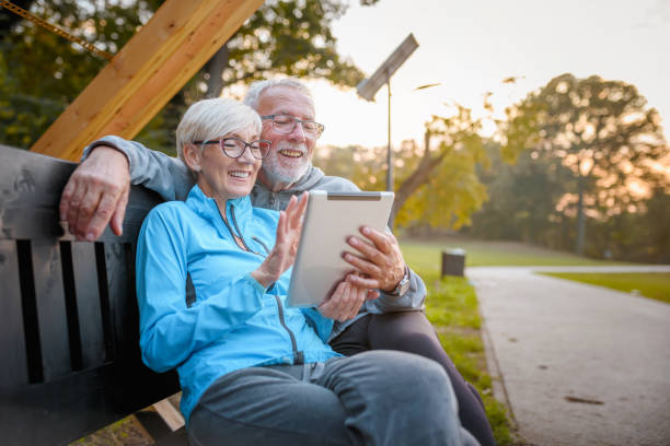 istock Smiling senior active couple sitting on the bench in the park looking at tablet computer. Using modern technology by elderly. 1352433447