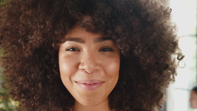 Slow motion video of a woman with afro hair opening eyes and smiling to the camera