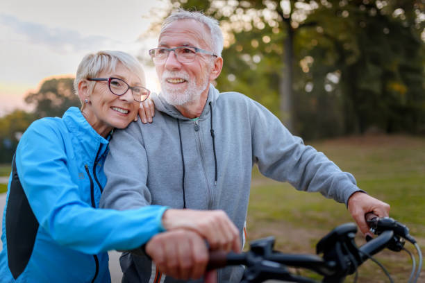 cheerful active senior couple with bicycles walking through park together. perfect activities for elderly people. - senior adult action cycling senior couple imagens e fotografias de stock