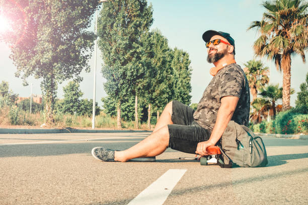 Curvy man in shorts sitting on a skateboard smiling.