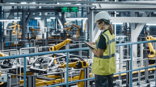 istock Female Car Factory Engineer in High Visibility Vest Using Tablet Computer. Automotive Industrial Manufacturing Facility Working on Vehicle Production with Robotic Technology. Automated Assembly Plant. 1352434632