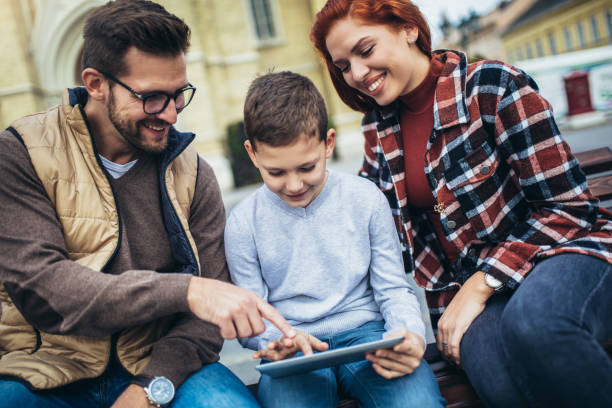 istock Family sitting on bench, relaxing using gadget, browsing internet. 1352434720