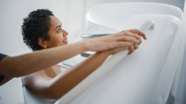 Friendly Female Doctor Explains the Mammogram Procedure to a Topless Latin Female Patient with Curly Hair Undergoing Mammography Scan. Healthy Female Does Cancer Prevention Routine in Hospital Room. Friendly Female Doctor Explains the Mammogram Procedure to a Topless Latin Female Patient with Curly Hair Undergoing Mammography Scan. Healthy Female Does Cancer Prevention Routine in Hospital Room. cancer screening stock pictures, royalty-free photos & images