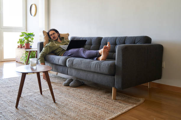 weite aufnahme eines jungen mannes, der auf dem sofa schläft, während er mit dem laptop arbeitet - ungesund leben stock-fotos und bilder