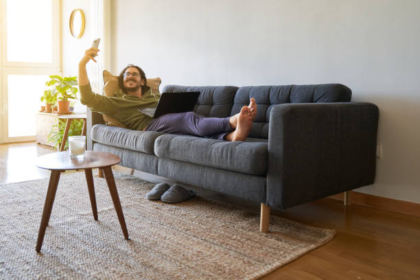 istock Wide shot of young man on the sofa taking selfie while using laptop 1352436337