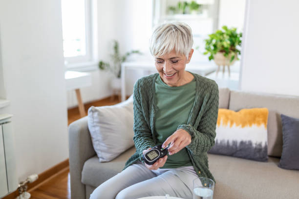 Happy mature woman with glucometer checking blood sugar level at home. Woman testing for high blood sugar. Woman holding device for measuring blood sugar Happy mature woman with glucometer checking blood sugar level at home. Woman testing for high blood sugar. Woman holding device for measuring blood sugar glucose photos stock pictures, royalty-free photos & images