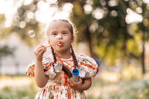 A girl with Down syndrome blows bubbles. The daily life of a child with disabilities. Chromosomal genetic disorder in a child.