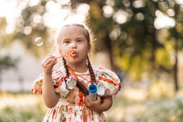 A girl with Down syndrome blows bubbles. The daily life of a child with disabilities. Chromosomal genetic disorder in a child. A girl with Down syndrome blows bubbles. The daily life of a child with disabilities. Chromosomal genetic disorder in a child. genetic research photos stock pictures, royalty-free photos & images