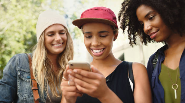 istock Shot of friends looking at something on a cellphone while standing outside 1352437849