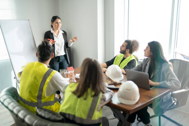 Architects talking about a new project in the office Businesswoman is talking about new project in the meeting room. Her team is sitting around a table and listening their manager carrefully. occupational safety and health stock pictures, royalty-free photos & images