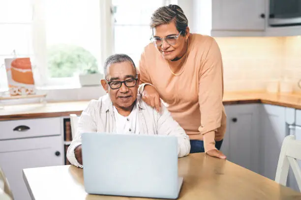 Photo of Shot of an elderly couple using a laptop in a kitchen at home