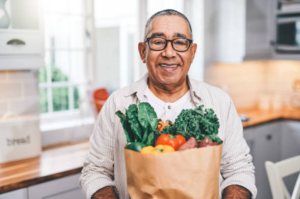shot of a elderly man holding a grocery bag in the kitchen - healthy food imagens e fotografias de stock