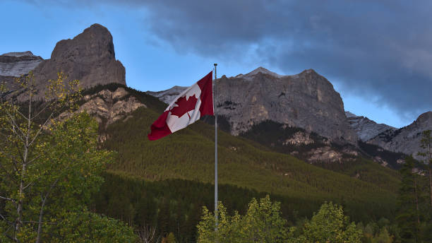 istock Huge red and white colored Canadian flag flying in the wind between trees in front of majestic mountains near Canmore, Kananaskis Country, Alberta, Canada in the Rockies. 1352443920