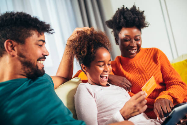 Happy african family having fun using credit card and digital tablet at home. stock photo