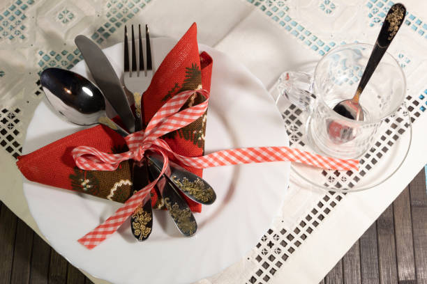 On a white napkin is a white plate with cutlery, a spoon, a fork and a knife tied with a red ribbon. Nearby is a cup with a teaspoon.