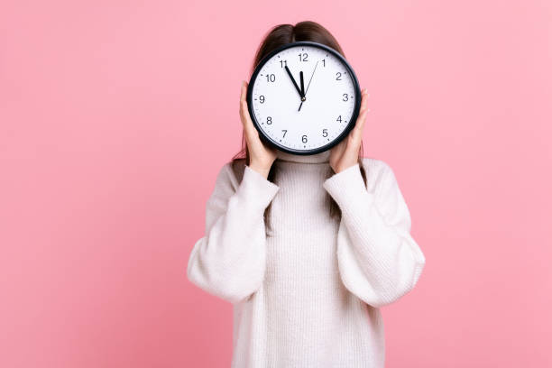 istock Unknown female hiding her face behind big wall clock, time management, schedule, meeting appointment 1352446390