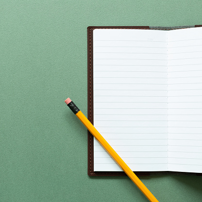 Open notebook and pencil on green background. top view, copy space