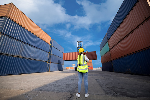 Portrait of asian woman foreman worker use walkie talkie for control driving folklife loading Containers box of walking area logistics corgo containers business services and industrial import export international concept