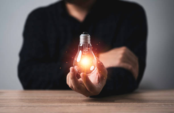 istock Businessman holding glowing light bulb with orange light ray on wooden table for inspiration creative thinking idea and future innovation technology  concept. 1352449743