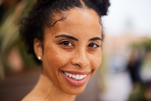 Close-up portrait of a confident young woman with freckles smiling while standing outside in summer