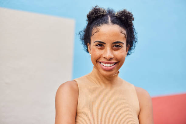 jeune femme souriante en se tenant devant un mur coloré à l’extérieur - sans manches photos et images de collection