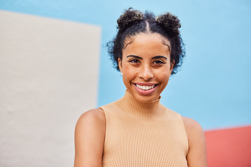 Portrait of a smiling young woman standing outside in front of a multi-colored wall in summer