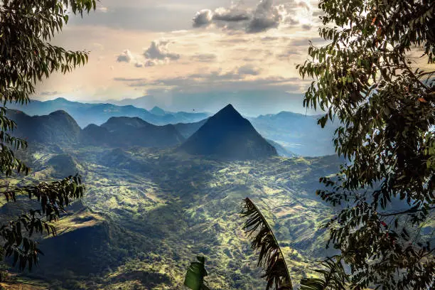 Epic landscape shot at early morning of large natural pyramid beyond the opening in the trees of Colombia shot from high altitude in the mountains of Antioquia, Colombia.
