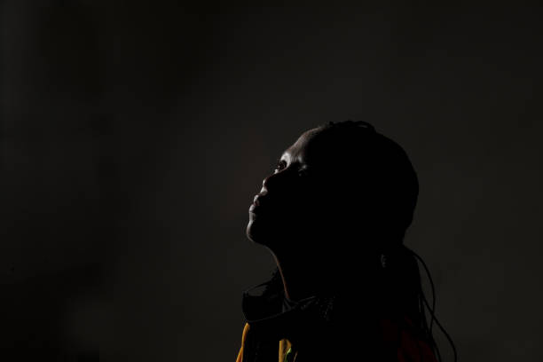 Studio image of black female. Studio image of black female. Only her outline of her face is highlighted and the rest of her face is in silhouette. woman alone dark shadow stock pictures, royalty-free photos & images