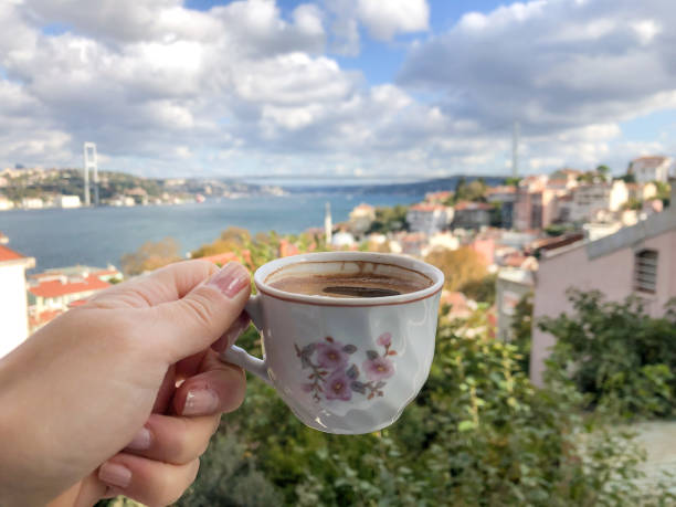 female hand holding a cup of coffee against sea and city view in a sunny day stock photo