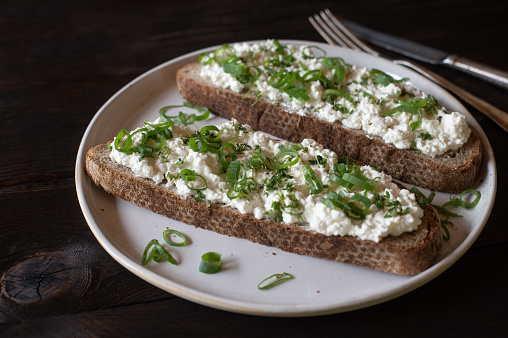 Delicious homemade and high protein fitness meal with german sourdough bread topped with low fat cottage cheese, chives and cress. Served on a plate isolated on wooden table.