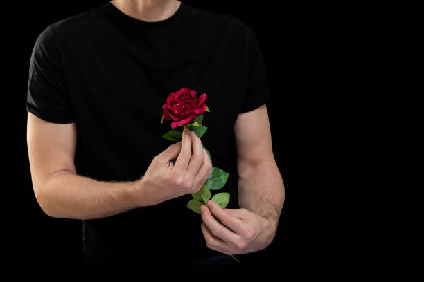 istock Handsome man hands with red rose flower on black background 1352457456