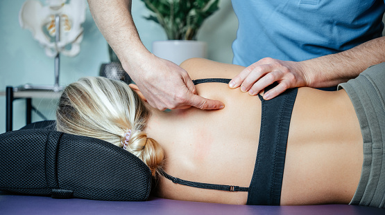 Osteopath pointing at rhomboid muscle before performing myofascial release technichue, treatment of shoulder blades (scapular) pain
