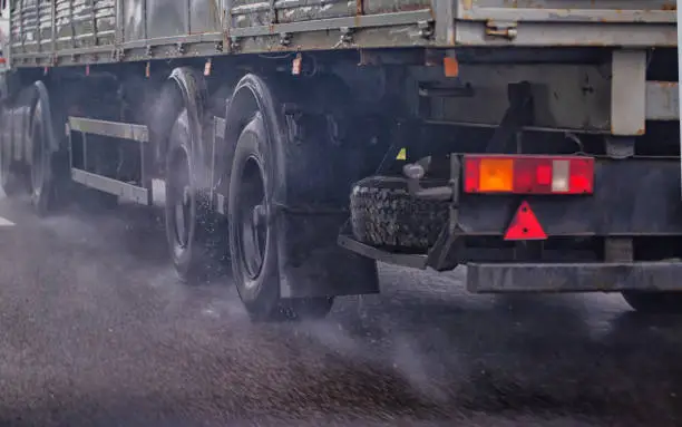 Wheels of a truck with a semi-trailer in the rain on a wet road. Tread grip on slippery road surfaces