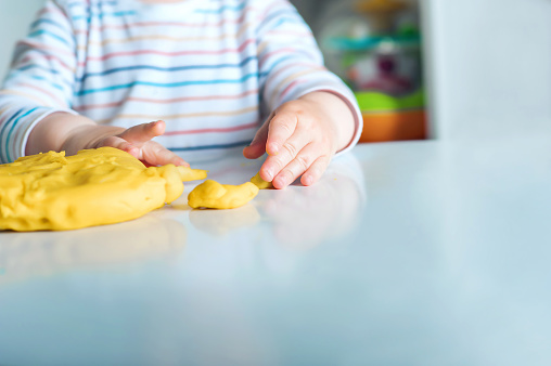 Toddler boy playing yellow plasticine Play-Doh in playroom close-up and copy space.