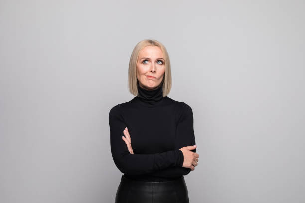 Portrait of displeased mature businesswoman Portrait of beautiful mature woman wearing black turtleneck, standing with arms crossed and looking away. Studio shot, grey background. high collar stock pictures, royalty-free photos & images
