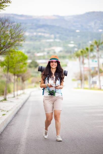 istock Cheerful young woman with backpack walking along asphalt road. 1352464088