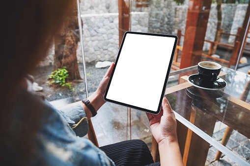 Mockup image of a woman holding digital tablet with blank white desktop screen in cafe