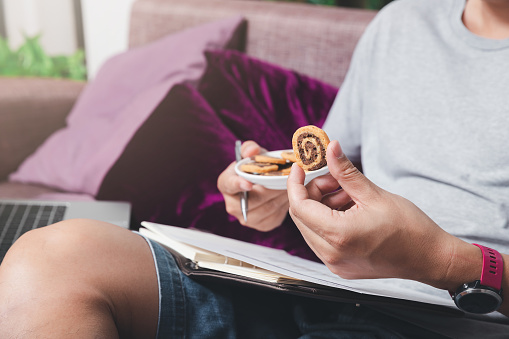 A man in casual wear picks up cookies while he is working at home office.