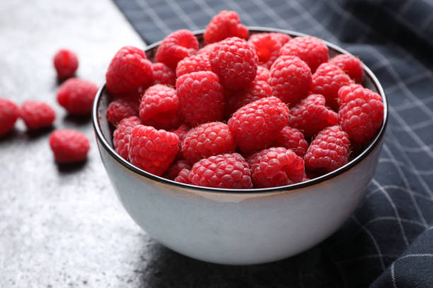 istock Delicious fresh ripe raspberries in bowl on grey table, closeup 1352471867