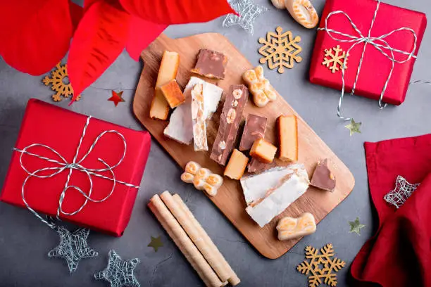 Traditional Spanish Christmas sweets turron, polvorones, mantecados with Christmas decor and red gift boxes on grey table top, copy space