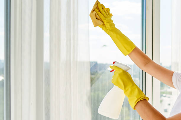 Close up of woman in yellow rubber gloves cleaning window with cleanser spray and yellow rag at home or office, copy space, back view. People, housework and housekeeping concept stock photo