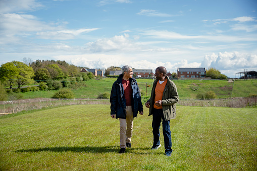 Male senior friends walking along a field together while on staycation laughing and talking together. They are enjoying retirement together, being active in the North East of England.