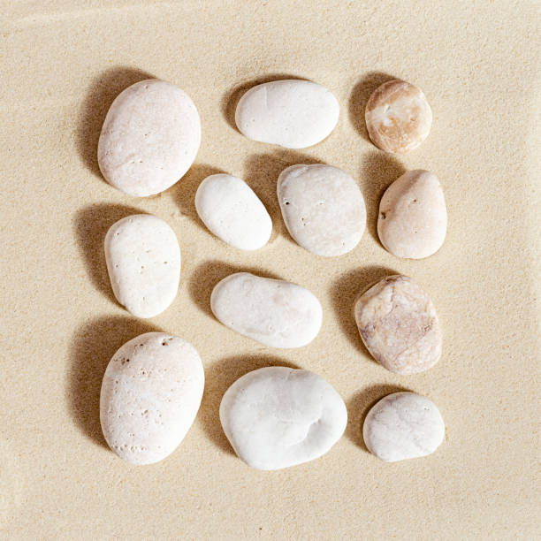 istock Pattern with white pebble sea stones on fine sand. Square composition from natural stone neutral beige color, monochrome tones 1352476223