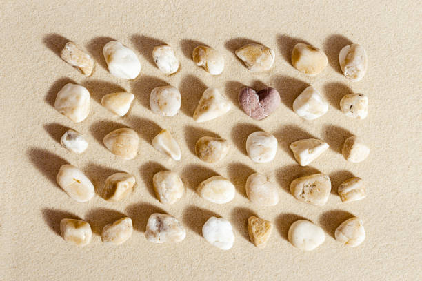 istock Aesthetic minimal pattern with set of pebble stones on fine sand background. Square composition from natural material with stone heart 1352476230