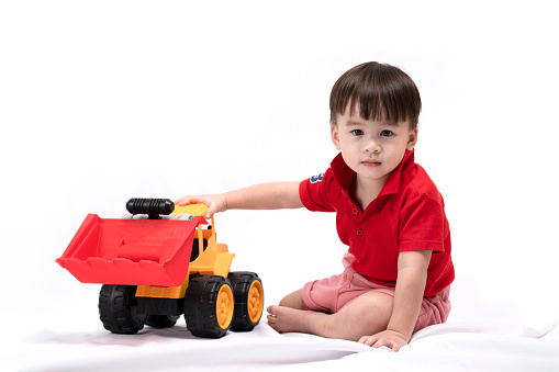 cute little boy sitting and playing toy excavator on white background. happy children playing toys