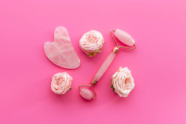 Pink gua sha massage stone with rose flowers for lifting face and wellness stock photo