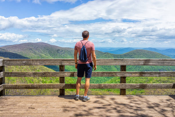 One young man with drawstring bag backpack standing on observation overlook deck wooden platform at Wintergreen ski resort town on nature Highlands leisure hiking trail, Virginia stock photo