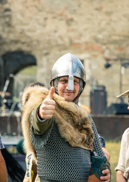 Photo of smiling knight male portrait in iron armor with helmet show thumbs up by hand, historical reconstruction and cosplay festival outdoor vertical photo